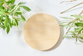 Empty round wooden podium for product presentation and green leaves on a light background. Mock up...
