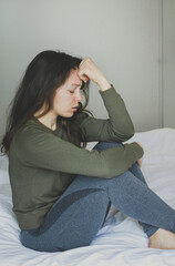 Upset depressed young brunette woman sitting on sofa at home. Feeling anxiety, thinking about life, relationships problem, unexpected pregnancy, experiencing grief, heartbreak. Vertical