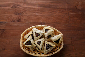 Gomentash with poppy seeds and prunes freshly baked for the Purim holiday on a wooden table in a wicker bread
