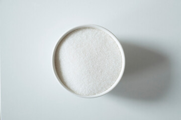 Granules of white sugar in a bowl on a white background