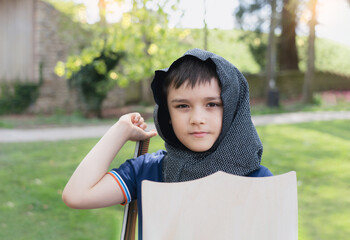 Young boy wearing knight costume holding sword shield standing in the park, Happy kid pretending to...