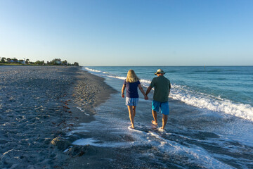 Retired couple walk down beach at sunrise in Florida