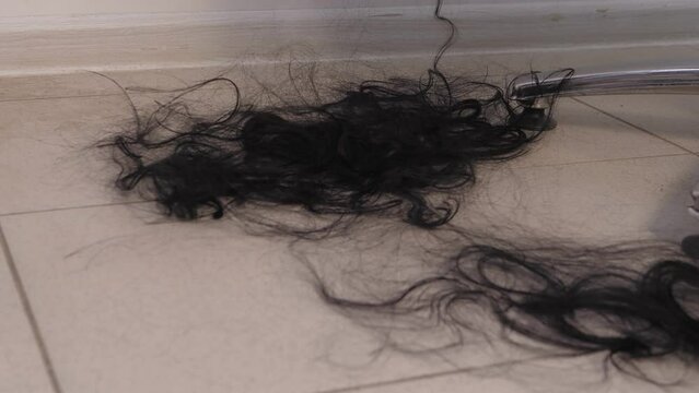 The long hair of a woman being shaved bald falls on the floor in the barbershop. Vertical panorama