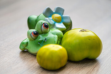 fresh and delicious green tomatoes and a green ceramic frog on a wooden table, closeup