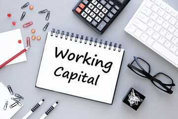 Working capital text on an open notepad on a gray background near the white pen glasses of a white keyboard