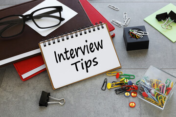 Interview Tips text on a notepad on two notepads near multi-colored paper clips.