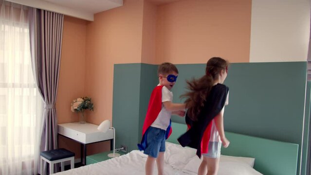 Girl and boy superheroes, are jumping in room on bed,in children's room, two children in red and blue Superman costume, Superheroes, brother and sister, play at home imagining they are superheroes.