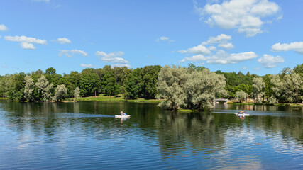 vacationers ride a boat on a forest lake against the backdrop of a park and blue sky