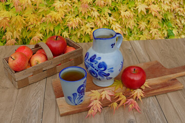 Ein Korb roter Äpfel mit Apfelwein in einem blauen Steingutkrug, Apfelwein eine Spezialität aus...