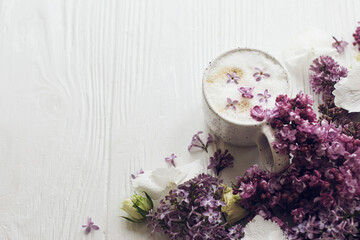 Delicious coffee with lilac petals, rose and lilac branch on rustic white wooden background. Hello spring. Space for text. Happy mothers day. Good morning.