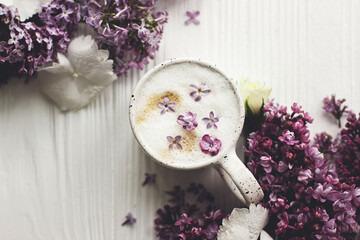 Delicious coffee with lilac petals and lilac branch on rustic white wooden background flat lay. Happy mothers day. Good morning, welcoming spring. Space for text