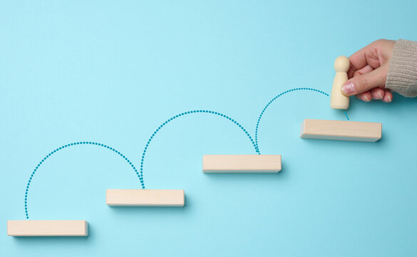 Wooden steps and a figurine of a little man in a woman's hand. Startup, starting a new successful business, achieving goals