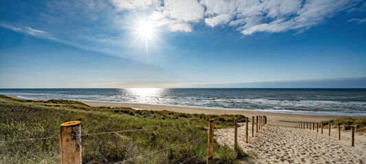 Ein Weg mit vielen Bahnen, begrenzt durch Holzpfähle auf der Sanddüne mit wildem Gras und Strand in Noordwijk an der Nordsee in Holland Niederlande - Panorama Meereslandschaft mit blauem Himmel und Wolken