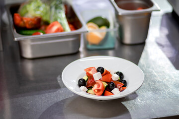 Freshly prepared Greek salad in a white plate lies on the kitchen table. Concept of сooking vegetarian salad
