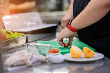 Obraz na płótnie Canvas The chef in the kitchen cuts a tomato for the chicken dish