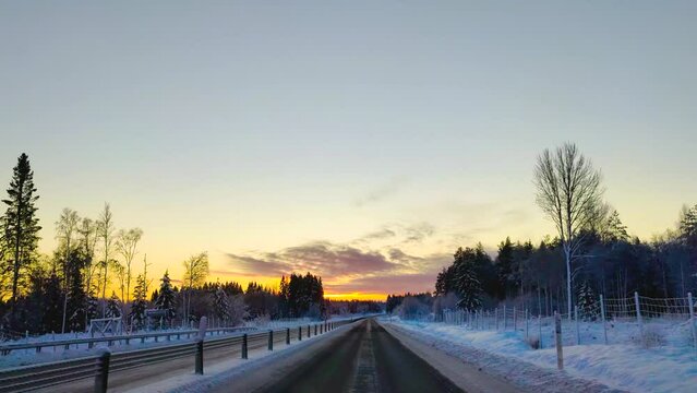 A drive on snow-covered road in 4K time-lapse. Clear sky horizon sunlight on the top of pine trees. hyperlapse dashcam view of car driving in winter landscape.