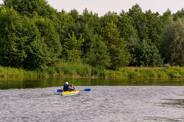 Fototapeta na wymiar Grodno, Belarus, June 2021: Two young girls kayak along the river along picturesque places. Kayak on the background of the forest. The concept of active recreation and healthy lifestyle