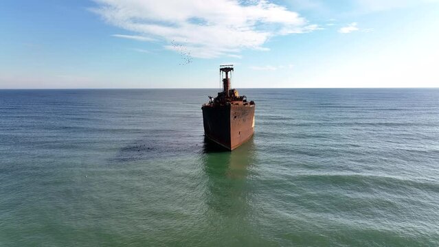 Flight over the shipwreck. 4K Aerial drone shot. A lone old ship wreck in the middle of the sea. Birds fly around the ship. Receding movement of a camera