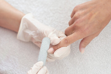 Manicurist uses nail file to nails. A woman is getting a manicure of nails. The beautician files the client's nails
