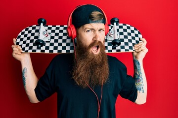 Redhead man with long beard holding skate wearing headphones clueless and confused expression....
