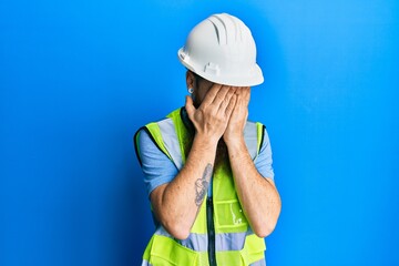 Redhead man with long beard wearing safety helmet and reflective jacket with sad expression...