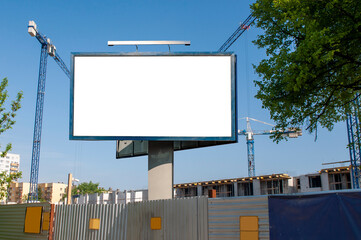 Blank white billboard for advertisement in front of the construction site. Apartment building under construction on a sunny day.