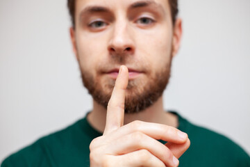 a young man covers his mouth with his finger, silence, do not talk