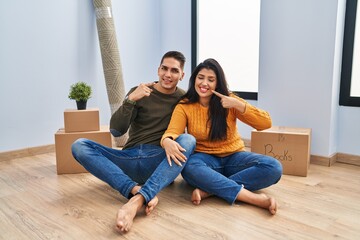 Young couple sitting on the floor at new home smiling cheerful showing and pointing with fingers teeth and mouth. dental health concept.