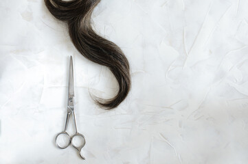 Top view of a strand of dark hair with scissors on a light marble background. copy space