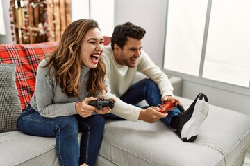 Young hispanic couple smiling happy sitting on the sofa playing video game at home.