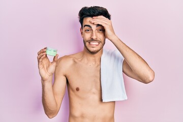 Fototapeta premium Young hispanic man shirtless wearing towel and eye bags patches stressed and frustrated with hand on head, surprised and angry face