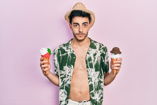 Young hispanic man wearing summer style holding ice cream relaxed with serious expression on face. simple and natural looking at the camera.