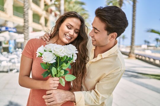 Man and woman couple holding bouquet of flowers hugging each other at seaside