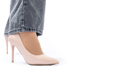 Women's legs in elegant patent leather high-heeled beige shoes. Gray wide leg jeans. Side view