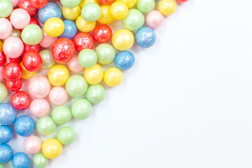 Multi-colored round glossy balls of sugar confectionery lie diagonally to the left on a white .