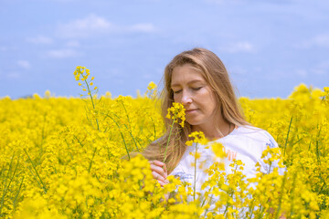 A fair-haired woman smells fragrant yellow flowers in a rapeseed field