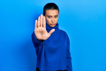 Beautiful hispanic woman with short hair wearing turtleneck sweater doing stop sing with palm of the hand. warning expression with negative and serious gesture on the face.