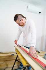 carpenter in protective glasses makes measurements and draws on wood
