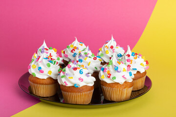 cupcakes with white frosting and colorful sprinkles placed on a round tray, set against a dual-color background.