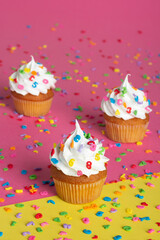 Cupcakes with creamy topping and colorful sprinkles on a two-tone pink and yellow backdrop.
