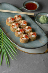 tempura sushi and rolls with red caviar on a black dish and gray background