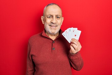 Handsome mature man playing poker holding cards looking positive and happy standing and smiling...