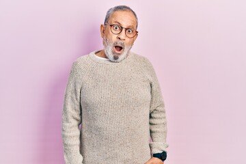 Handsome senior man with beard wearing casual sweater and glasses in shock face, looking skeptical...