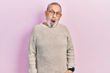 Obraz premium Handsome senior man with beard wearing casual sweater and glasses in shock face, looking skeptical and sarcastic, surprised with open mouth