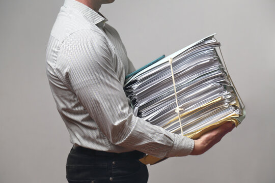  Impiegato con fatica tiene tra le braccia un enorme fascicolo di documenti ed uno smartphone 