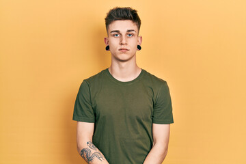 Young caucasian boy with ears dilation wearing casual green t shirt with serious expression on face. simple and natural looking at the camera.