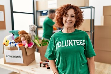 Middle age woman wearing volunteer t shirt at donations stand winking looking at the camera with...