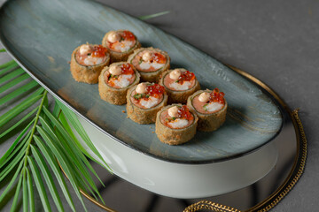 tempura sushi and rolls with red caviar on a black dish and gray background