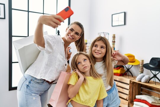 Mother and daughters make selfie by the smartphone holding shopping bags at clothing store