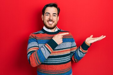 Fototapeta premium Handsome caucasian man with beard wearing elegant wool winter sweater amazed and smiling to the camera while presenting with hand and pointing with finger.